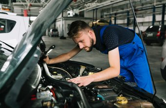 Mechaniker inspiziert konzentriert den Motorraum eines Fahrzeugs in der Werkstatt.